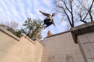 ein junger mann macht einen sprung durch den raum zwischen den betonbrüstungen. Der Athlet übt Parkour und trainiert unter Straßenbedingungen. das Konzept der sportlichen Subkulturen unter Jugendlichen foto