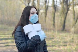 Covidiotisches Konzept. junge frau in schutzmaske hält im frühlingsholz viele rollen toilettenpapier im freien foto