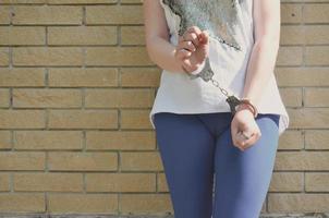 Fragment des Körpers eines jungen kriminellen Mädchens mit Händen in Handschellen vor einem gelben Backsteinmauerhintergrund. das Konzept der Inhaftierung eines Täters einer weiblichen Kriminellen in einer städtischen Umgebung foto