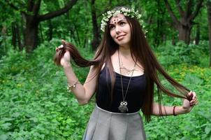 Porträt eines emotionalen jungen Mädchens mit einem Blumenkranz auf dem Kopf und glänzenden Ornamenten auf der Stirn. süße Brünette posiert tagsüber an einem schönen Tag in einem aufkeimenden schönen Wald foto