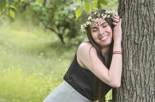 ein waldbild einer schönen jungen brünetten europäischer ausstrahlung mit dunkelbraunen augen und großen lippen. auf dem Kopf des Mädchens trägt sie einen Blumenkranz, auf der Stirn glänzende Verzierungen foto