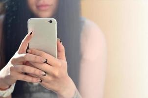 Das brünette Mädchen benutzt ein modernes Touch-Smartphone foto