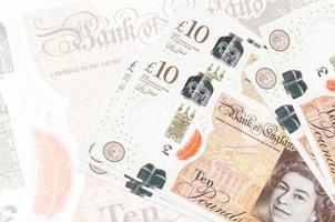 10 britische Pfund-Scheine liegen im Stapel auf dem Hintergrund einer großen halbtransparenten Banknote. abstrakte Darstellung der Landeswährung foto