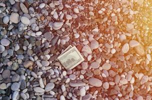 Hundert Dollar, die halb mit runden Felsen bedeckt sind, liegen am Strand foto