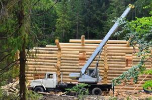 der Prozess des Baus eines Holzhauses aus Holzbalken mit zylindrischer Form. Kran in funktionstüchtigem Zustand foto