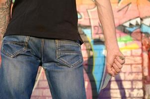 Rückansicht des jungen kaukasischen Mannes mit Messer in der Hand gegen Ghetto-Ziegelwand mit Graffiti-Gemälden. konzept der kriminellen kräfte und aggressionsvorwürfe foto