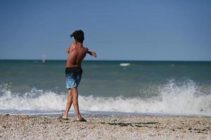 Rückseite des Jungen wirft Kieselsteine ins Meer am Strand von Porto Sant Elpidio, Italien. foto