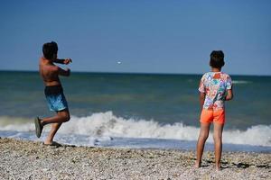 zwei brüder werfen am strand von porto sant elpidio, italien, kieselsteine ins meer. foto