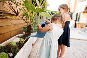 Zwei Schwestern mit Dose gießen die Blumen auf der Terrasse des Hauses. foto