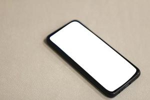 ein schwarzes handy mit einem leeren weißen bildschirm steht auf einer bank, die mit einem strukturierten stoff bezogen ist. geeignet für Handy- oder Gadget-Modelle foto