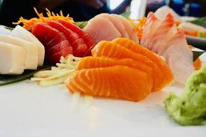 verschiedene Menüs, Sushi, Sashimi, Nigiri, gebratenes Schweinefleisch und Miso-Suppe. sashimi, chutoro sashimi, japanische essensstäbchen und wasabi auf dem schwarzen tisch, japanischer essensstil. verwischt den Fokus. foto