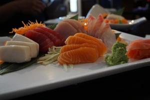 verschiedene Menüs, Sushi, Sashimi, Nigiri, gebratenes Schweinefleisch und Miso-Suppe. sashimi, chutoro sashimi, japanische essensstäbchen und wasabi auf dem schwarzen tisch, japanischer essensstil. verwischt den Fokus. foto