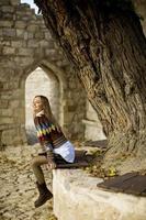 Junge Frau, die auf der Bank sitzt und gelbe Blätter im Herbstpark beobachtet foto