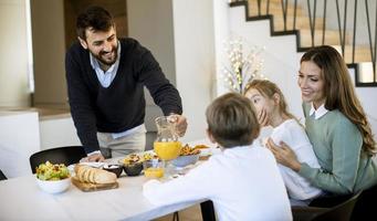 junge glückliche familie, die beim frühstücken am esstisch spricht foto