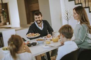 junge glückliche familie, die beim frühstücken am esstisch spricht foto