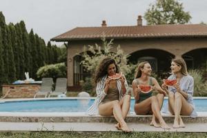 junge Frau sitzt am Swimmingpool und isst Wassermelone im Hinterhof des Hauses foto