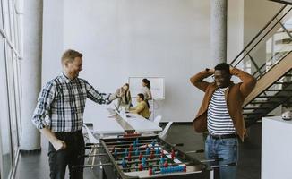 Junge lässige multiethnische Geschäftsleute, die Tischfußball spielen und sich im Büro entspannen foto