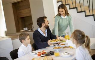 junge glückliche familie, die beim frühstücken am esstisch spricht foto