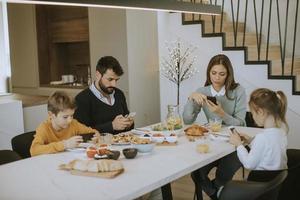 familie, die handys benutzt, während sie am esstisch in der wohnung frühstücken foto