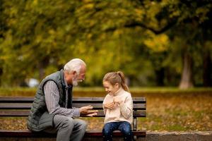 großvater, der am herbsttag mit seiner enkelin im park rote hände schlägt foto