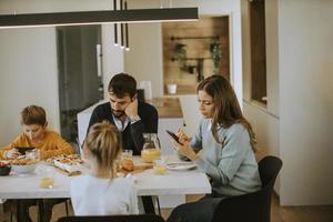 familie, die handys benutzt, während sie am esstisch in der wohnung frühstücken foto