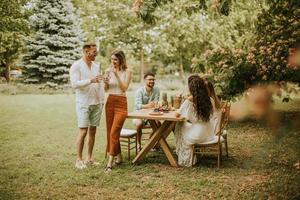 gruppe glücklicher junger leute, die mit frischer limonade jubeln und früchte im garten essen foto