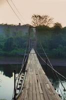 alte Holzbrücke aus goldenem Teak für einen ländlichen Streifzug über den Fluss in einer wunderschönen Morgensonne voller Wälder. foto