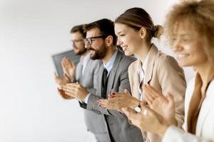 Gruppe verschiedener junger Mitarbeiter, die in einer Reihe stehen und im Büro applaudieren foto