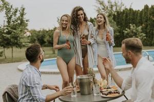 Gruppe junger Leute, die mit Getränken jubeln und Obst am Pool im Garten essen foto