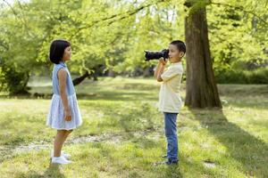 kleiner asiatischer junge, der sich wie ein professioneller fotograf verhält, während er fotos von seiner kleinen schwester macht
