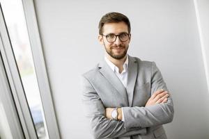 Junger moderner Geschäftsmann, der im Büro an der Wand steht foto