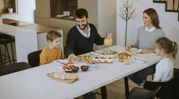 junge glückliche familie, die beim frühstücken am esstisch spricht foto