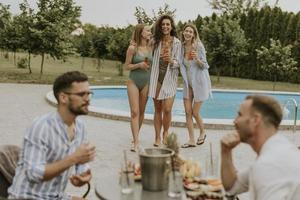 Gruppe junger Leute, die mit Getränken jubeln und Obst am Pool im Garten essen foto