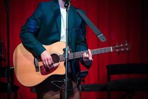 Mann spielt klassische Gitarre gegen roten Vorhang foto