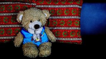 Teddybär in einem blauen T-Shirt auf einem schwarzen Sofa foto