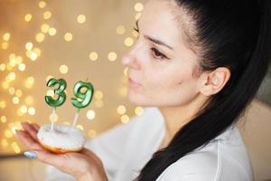 frau, die einen kuchen mit den kerzen der nummer 39 auf festlichem unscharfem bokeh-hintergrund hält foto