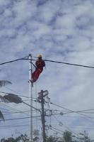 gorontalo-indonesien, dezember 2022 - techniker schließen kabel an strommasten an. Mitarbeiter, der am Gürtel am Strommast hängt, um Niederspannungskabel zu verlegen foto