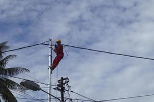 gorontalo-indonesien, dezember 2022 - techniker schließen kabel an strommasten an. Mitarbeiter, der am Gürtel am Strommast hängt, um Niederspannungskabel zu verlegen foto