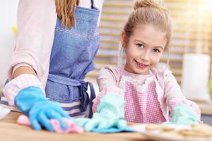 Kleines Mädchen und ihre Mutter in Schürzen putzen die Küche foto