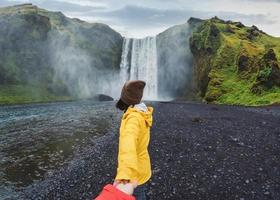 asiatische frau, die hände mit paar vor dem skogafoss-wasserfall hält, der im sommer auf island auf einer klippe fließt foto