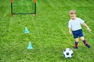 kleiner Junge, der draußen Fußball übt foto