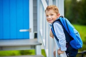 glücklicher kleiner vorschulkindjunge mit rucksack, der draußen aufwirft foto