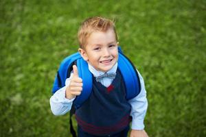 glücklicher kleiner vorschulkindjunge mit rucksack, der draußen aufwirft foto