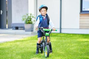 schuljunge im schutzhelm, der fahrrad mit rucksack fährt foto