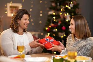 schönes paar, das geschenke während des weihnachtsessens teilt foto