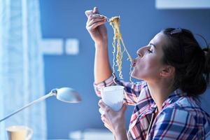 hungriger student, der nudeln isst, während er zu hause lernt foto