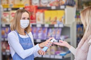 erwachsene frau in medizinischer maske mit handdesinfektionsmittel vor dem einkauf von lebensmitteln foto