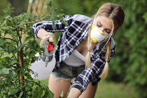 Erwachsene Frau sprüht Pflanzen im Garten, um sich vor Krankheiten zu schützen foto