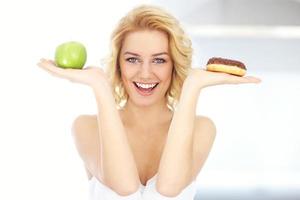 glückliche frau, die zwischen donut und apfel wählt foto