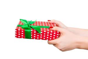 frauenhände geben eingewickeltes weihnachts- oder anderes handgemachtes geschenk in rotem papier mit grünem band. isoliert auf weißem Hintergrund, Ansicht von oben. Thanksgiving-Geschenkbox-Konzept foto